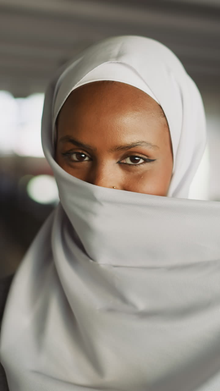 Happy black woman hides face behind hijab fabric for joke under bridge at city riverside slow motion. Traditional Islamic female accessory in urban fashion