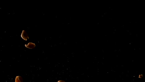 slow motion shot of salted peanuts falling on the camera in a studio shot with a black background