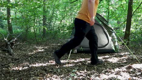 tourist man adjusting the tent sides at a campsite in the woods