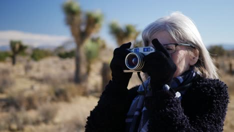 an adult woman photographer taking pictures with her old fashioned film camera in a desert wildlife landscape