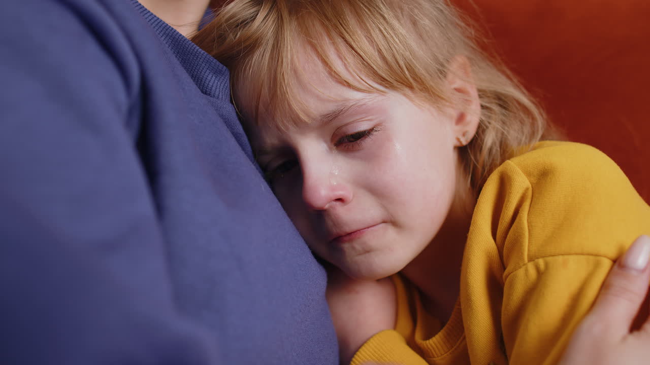 Upset child little girl kid crying with tears flowing down on cheek toddler lies on mother at home