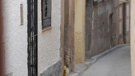 handheld medium black cow from running on street at traditional celebration, encierro, in spain. village one-storey town houses, visible brick on walls. metal gate on doors, windows.