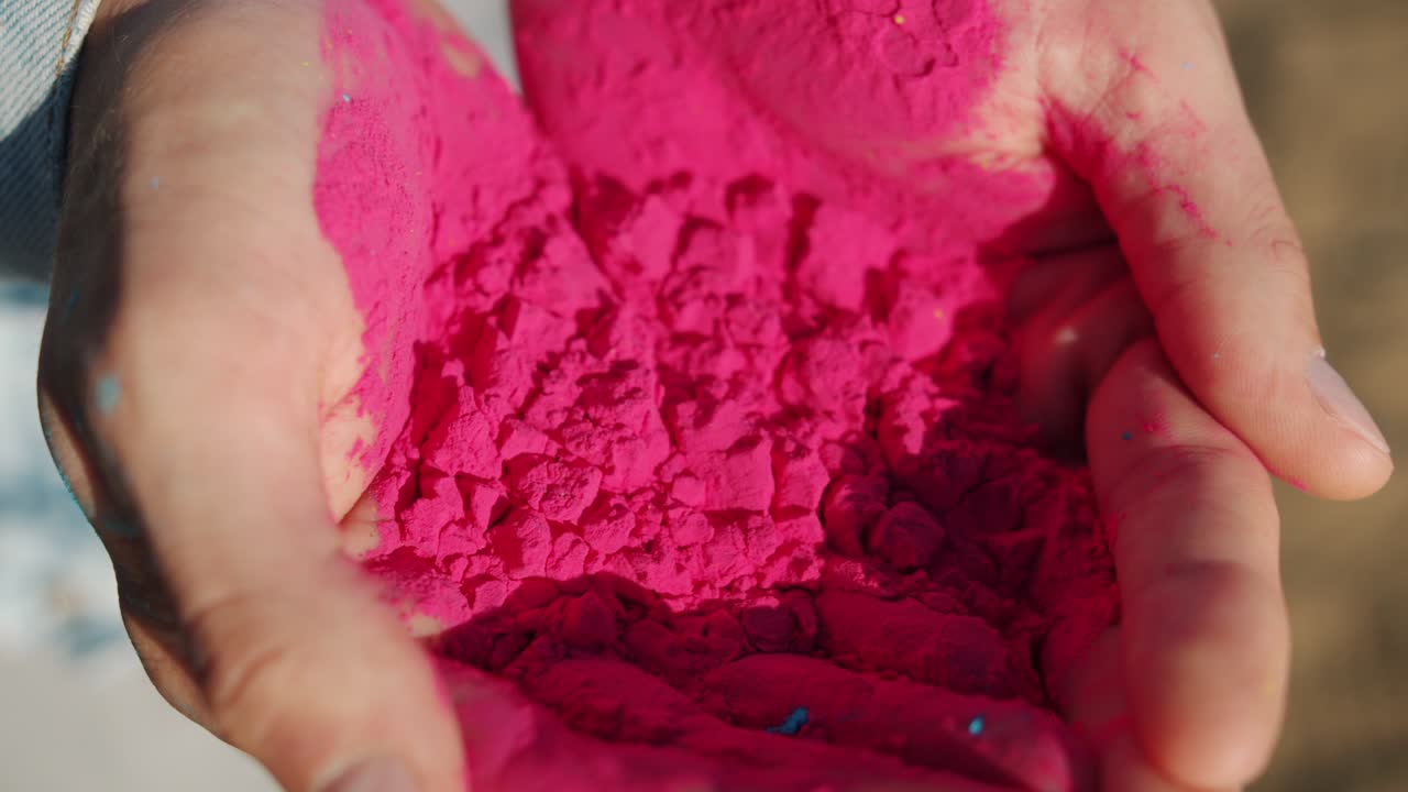 Nærbillede af hænder, der holder lyserødt gulal-farvet pulver til Holi-festivalen, klar til udendørs fejring.
