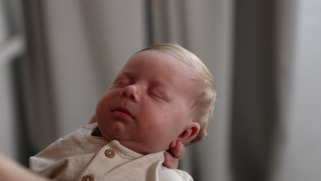caucasian newborn looking unhappy. baby boy sleeping in parent's hands. close up.