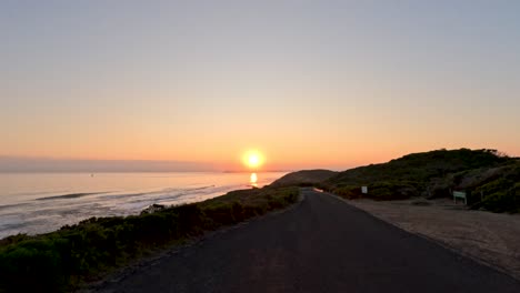 a serene sunset over the ocean, viewed from a coastal road on mornington peninsula, with vibrant colors and calm atmosphere