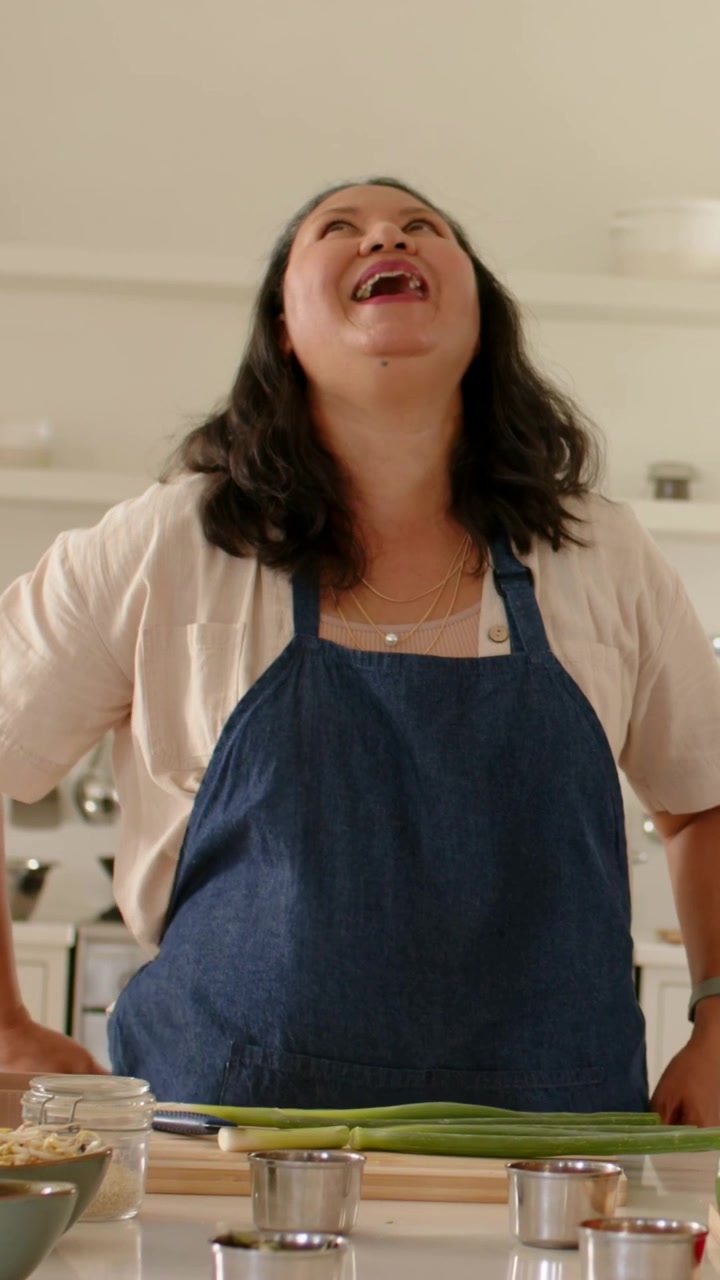 Video verticale: Cuoco con grembiule che mostra una ricetta, risponde a un segnale e ride in cucina con le cipolle.