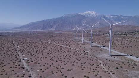 drone pulls back, revealing windmills in desert with snow-capped mountains in background