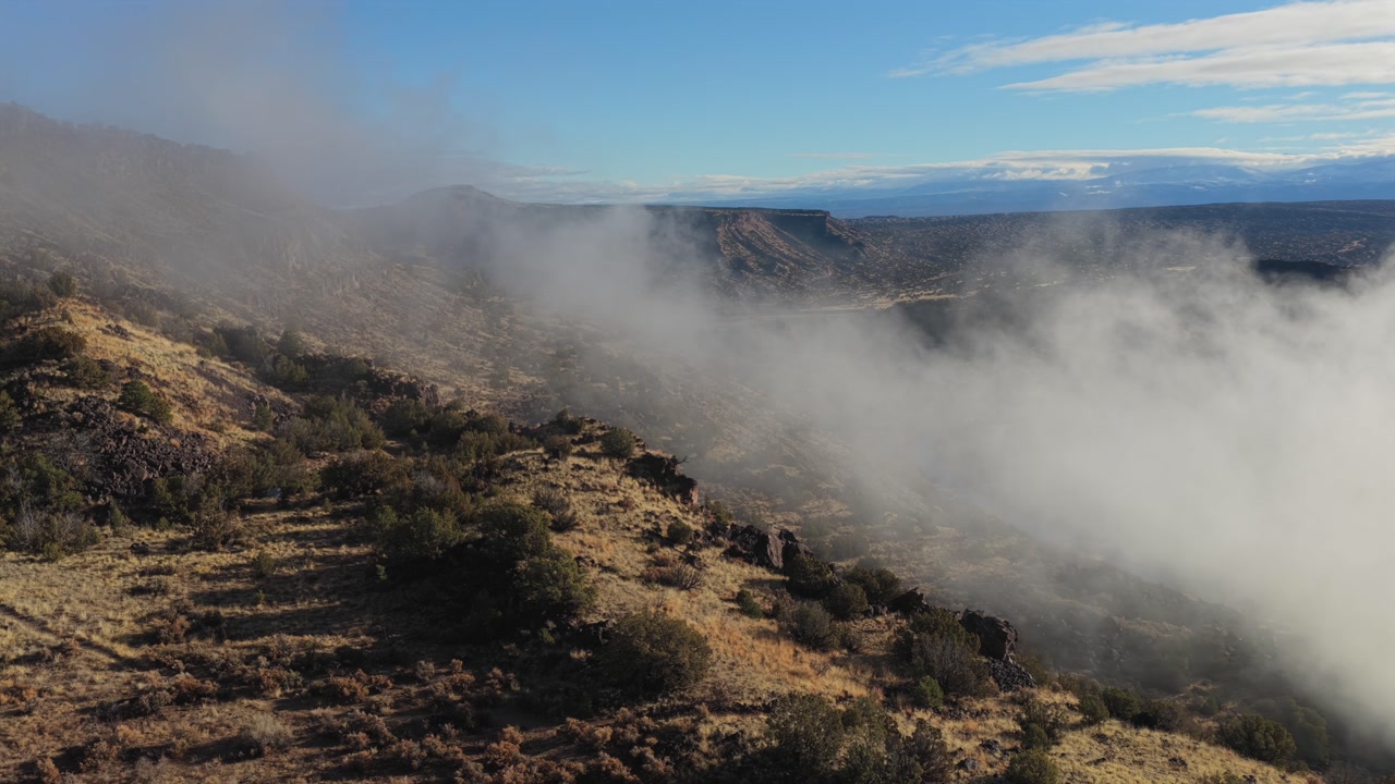 Drone shot of thick mist captured forming and swirling within a deep canyon gorge. This aerial view shows the natural development of clouds over a rugged and rocky remote wilderness environment.