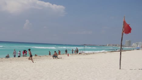 Bandera-Roja-En-La-Playa-En-Primer-Plano,-Un-Niño-Corriendo-En-La-Parte-De-Atrás-En-Dirección-Al-Océano