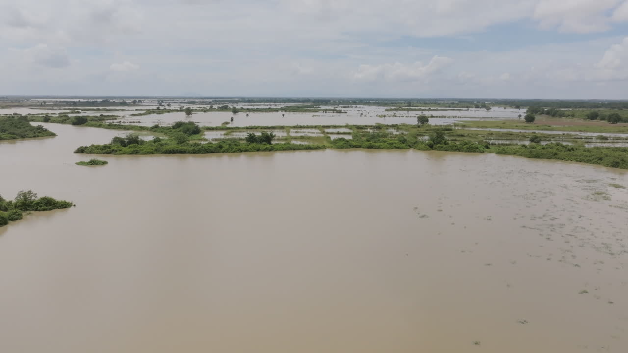 Wide aerial shot of flooded plains in Cambodia, with patches of green vegetation scattered between muddy water channels