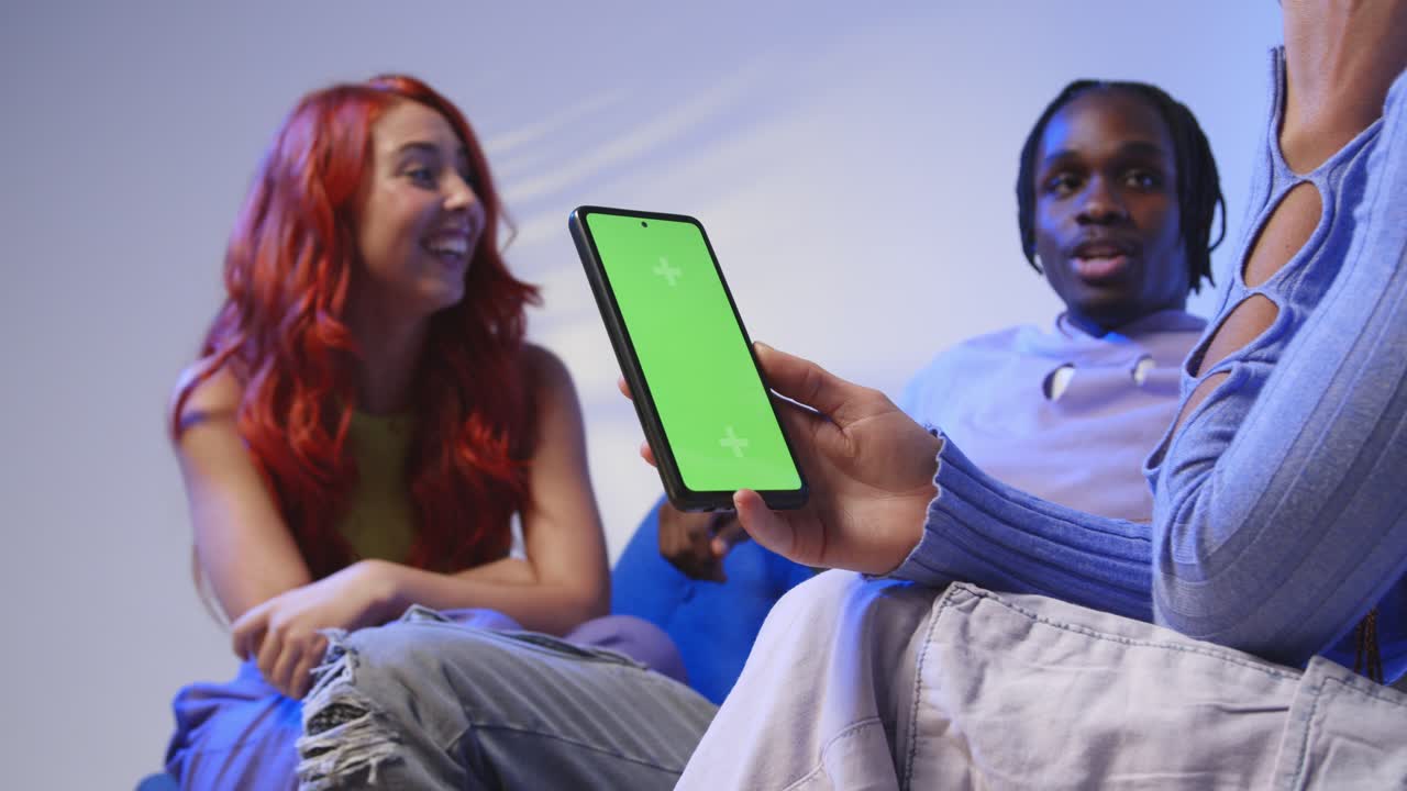 primer plano de una mujer con un teléfono móvil de pantalla verde sentada con amigos de la generación z hablando y compartiendo publicaciones 5