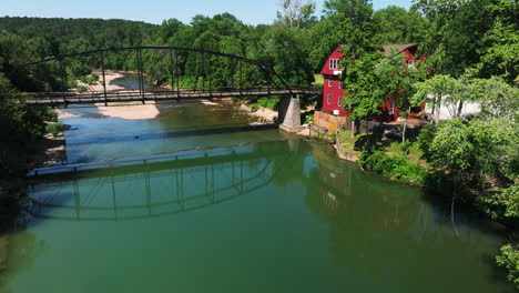 Peaceful-scenery-of-War-Eagle-Creek-with-bridge-and-mill-facing-water,-aerial