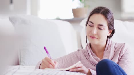 happy caucasian woman sitting on floor and taking notes on couch