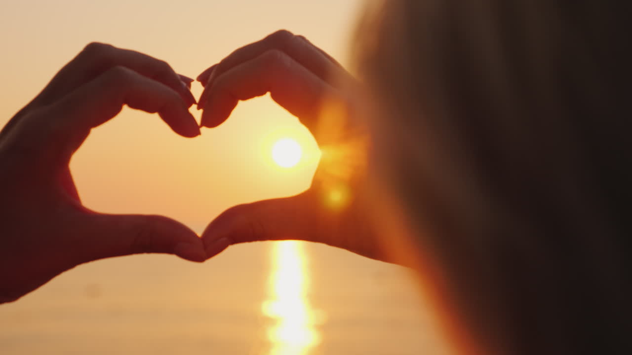 las manos de una mujer muestran un símbolo de corazón sobre el mar donde el sol sale por encima del agua de rosas amor y ho