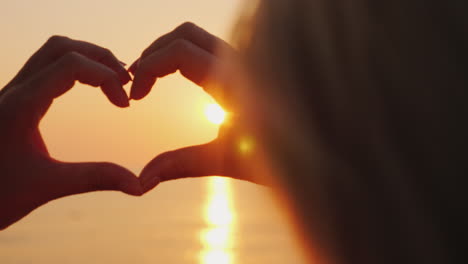 a woman hands shows a heart symbol over the sea where the sun rises above the rose water love and ho