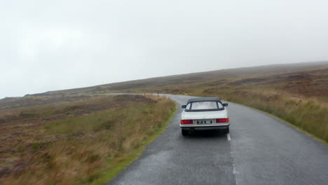 Seguimiento-Hacia-Adelante-De-La-Conducción-De-Automóviles-Deportivos-Antiguos-Plateados-En-Carreteras-Mojadas-A-Lo-Largo-De-Páramos.-Clima-Brumoso-De-Otoño.-Irlanda