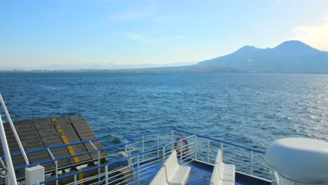 italian flag blowing in the wind on boat ride across mediterranean sea with mount vesuvius on the side leaving naples, italy