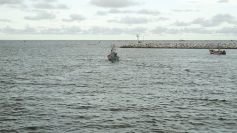 una foto de un pequeño bote pesquero tailandés que sale de la boca del puerto deportivo en khao takiab, las aguas oceánicas del golfo de tailandia se encuentran con el horizonte en la distancia en una noche nublada, hua hin, tailandia