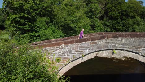 tracking aerial shot of man walking over arched bridge left to right