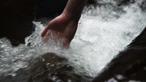 person puts their hand in fast flowing stream of water as it passes between rocks