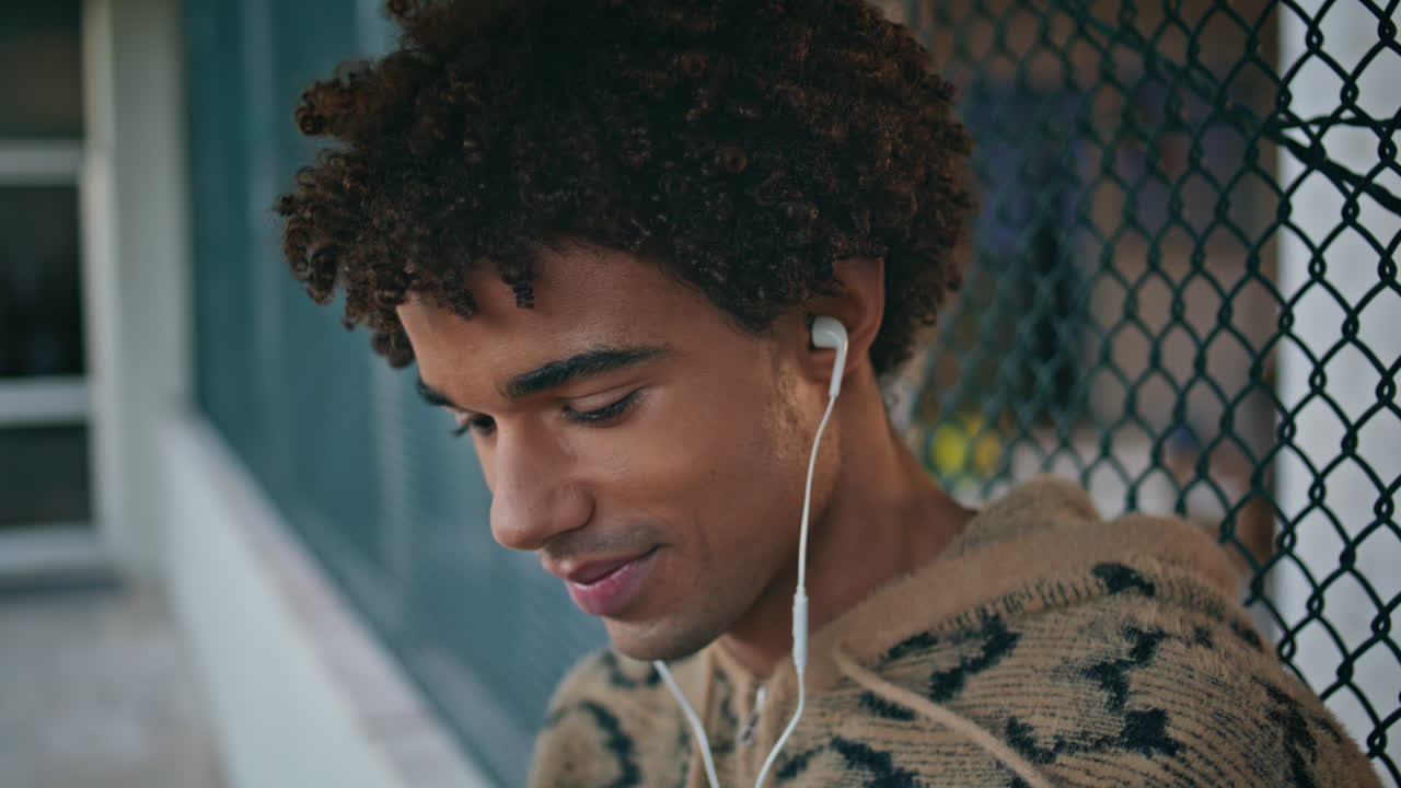 Adolescente sorridente ouvindo música com fones de ouvido em uma área urbana tranquila, close-up.