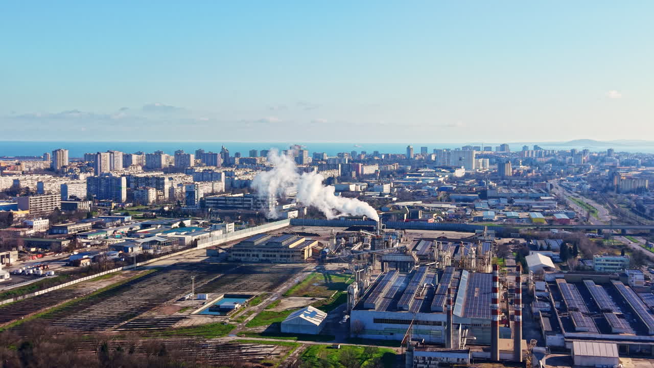 View of a city skyline showing factories and buildings with smoke rising near the coast on a clear day