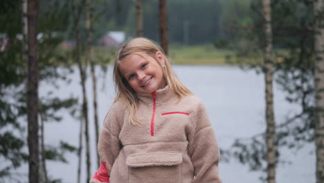 Cheerful-cute-blonde-little-girl-looking-at-camera-in-outdoor-forest-environment