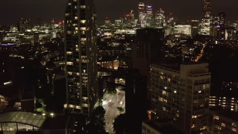 Tilt-up-reveal-of-downtown-skyscrapers-at-night.-Aerial-view-of-street-leading-between-apartment-buildings.-London,-UK