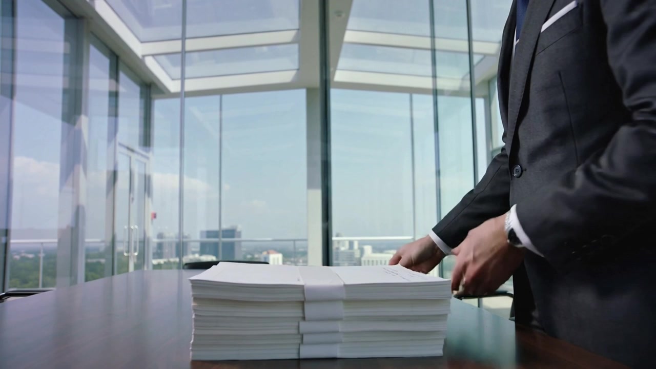 Lifting sheet suit exec stacking reams in glass office topping brown folder for meeting, copy space