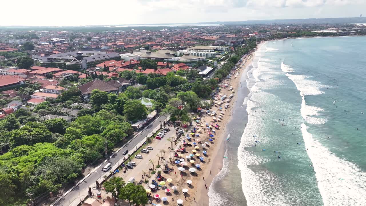 Aerial of Kuta Beach in Bali, busy beach and road lined by trees and hotels. Indonesia holiday