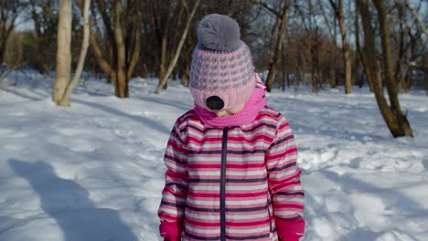 Child-girl-looking-at-camera,-starting-laughing,-fooling-around,-smiling-in-winter-snow-park-forest