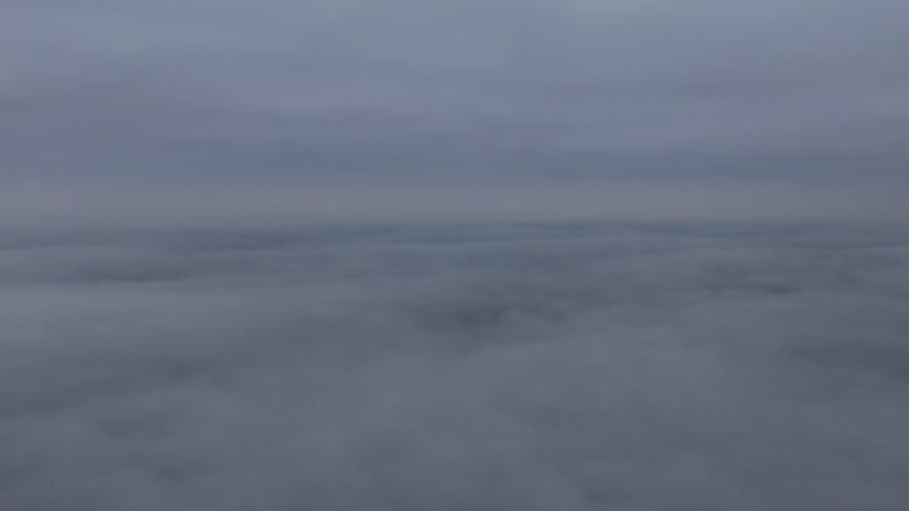 Drone footage above a thick cloud layer on an overcast day, showing a calm, uniform blanket of grey clouds with soft atmospheric light and no visible landscape