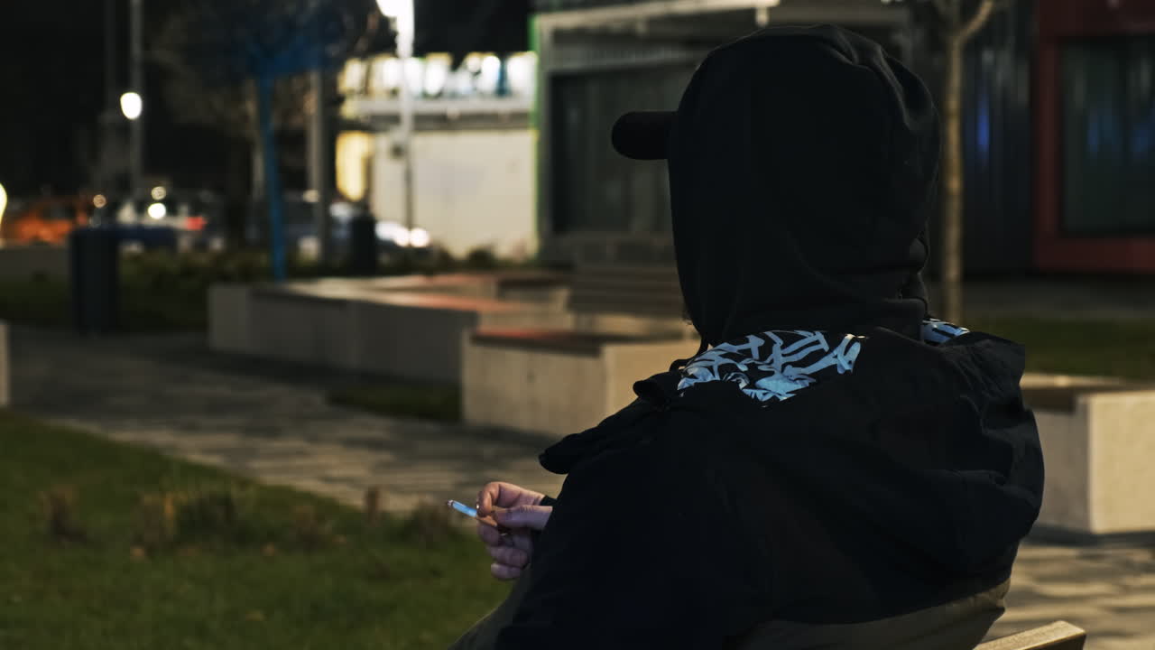 A man in black hood smoking on the street at night in Bucharest, Romania
