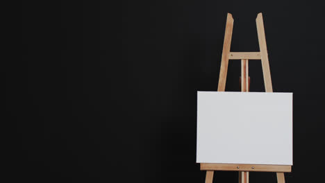 video of white canvas sign on wooden easel with copy space on black background