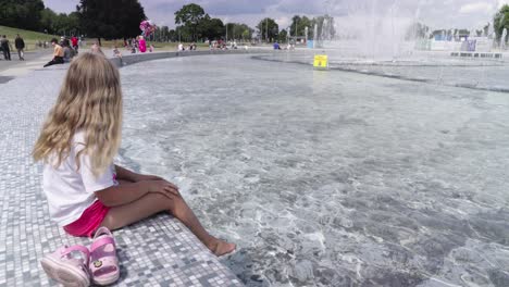 una niña se sumerge con los pies descalzos en la fuente de la ciudad en el centro de varsovia