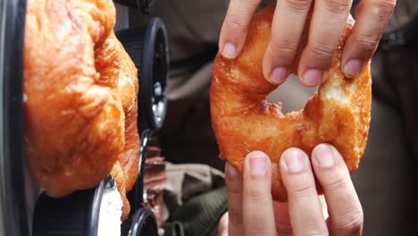 close-up of hands holding and eating a freshly fried doughnut