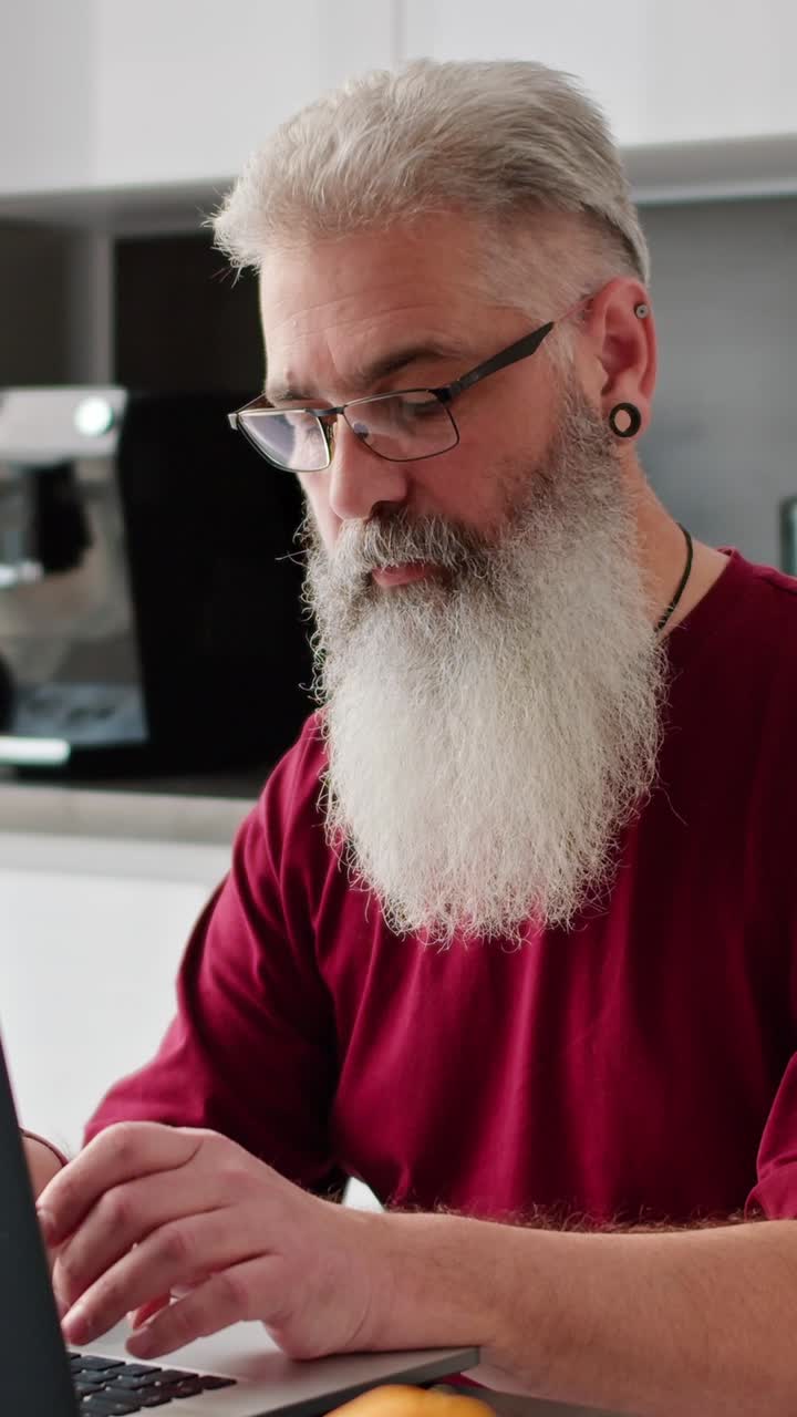 Older man working on laptop in kitchen