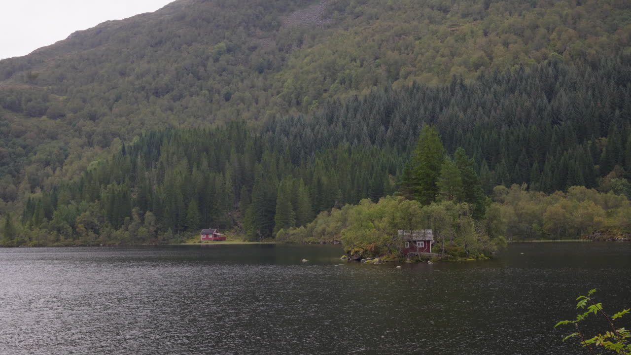 Landscape with two wooden cabins in the norwegian mountains. Surrounded by a lake and pine forrest. This scene captures the an essence of the scandinavian nature.