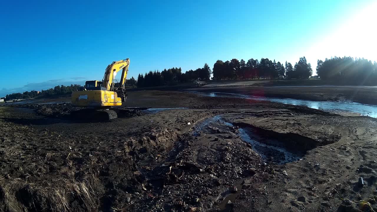 Yellow Excavator Works with Bucket to Clear Mud Sludge and Debris from the bottom of the Drained River.