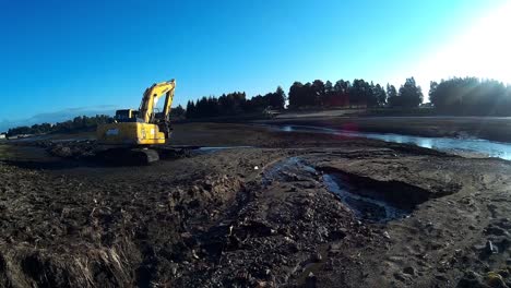 yellow excavator works with bucket to clear mud sludge and debris from the bottom of the drained river.