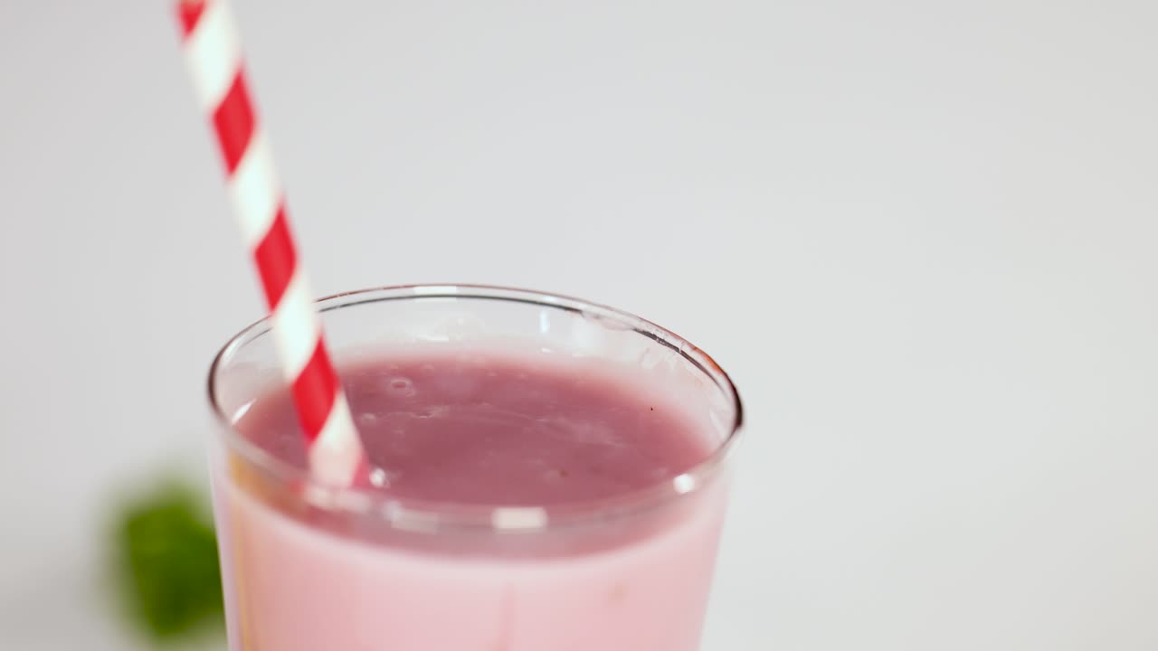 Hand places fresh strawberry garnish on pink smoothie in glass with striped straw, bright lighting