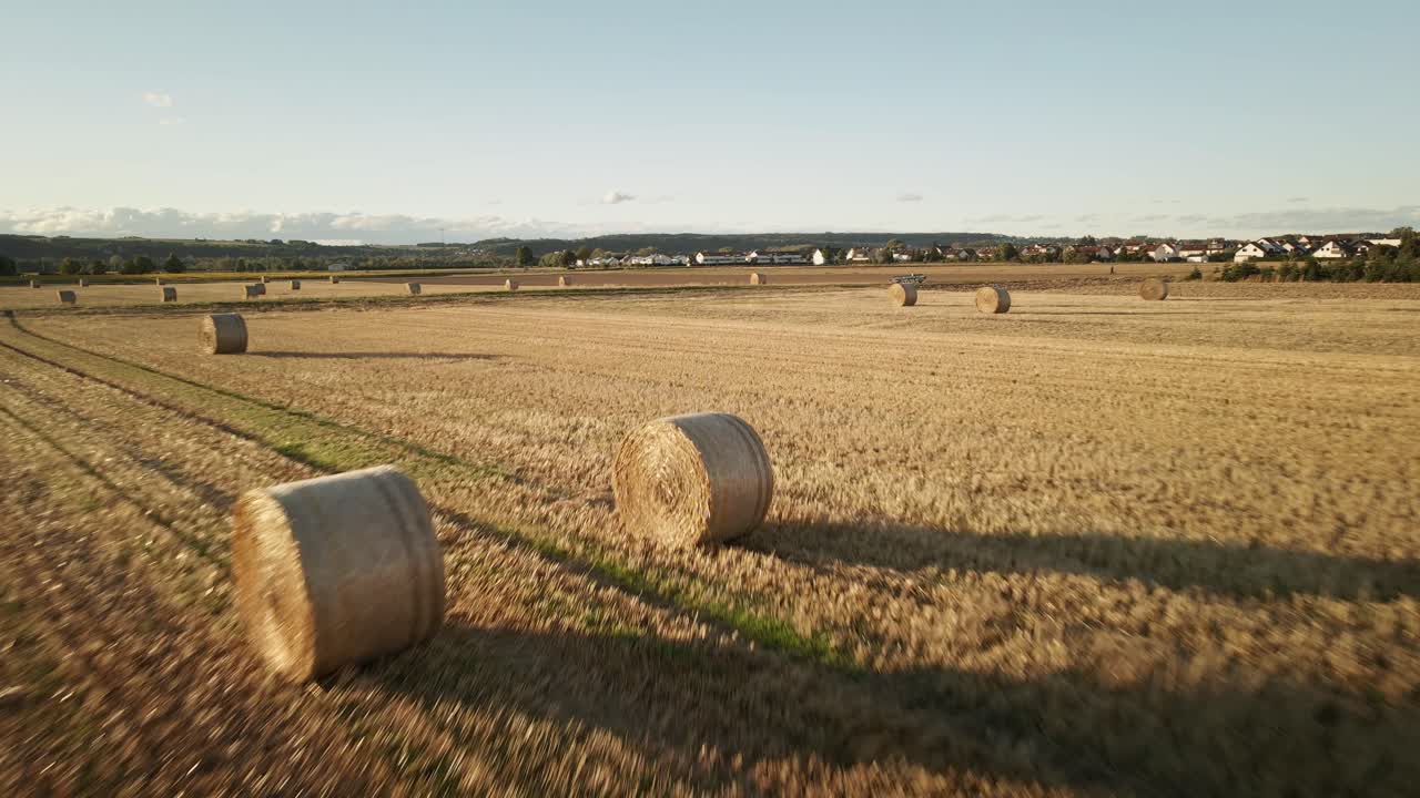 Low-altitude drone footage showcasing rolled hay bales neatly spread across an open field, capturing the textures of rural farmland and golden tones of harvest.