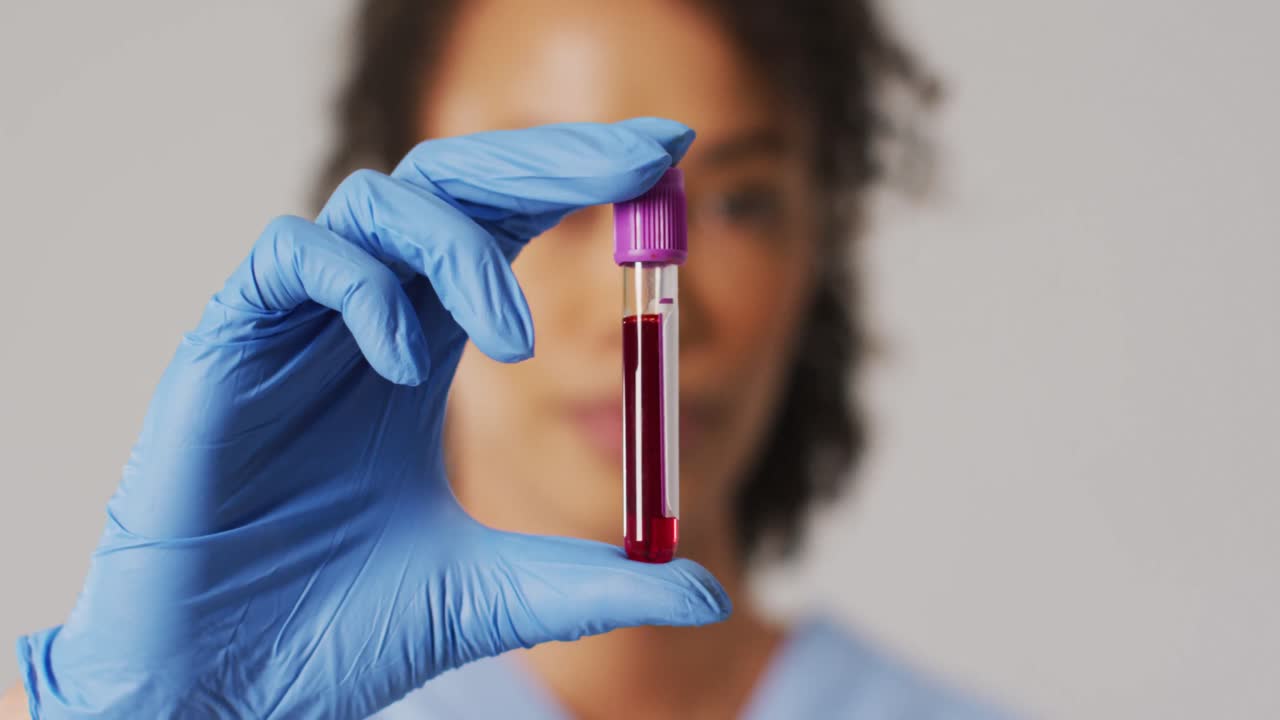 video de una doctora biracial sosteniendo un tubo de ensayo sobre un fondo azul