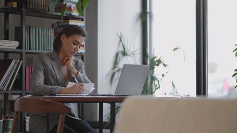 businesswoman analyzing the graph and typing on laptop. remote job young female in eyeglasses writes notes in clipboard and typing on laptop keyboard