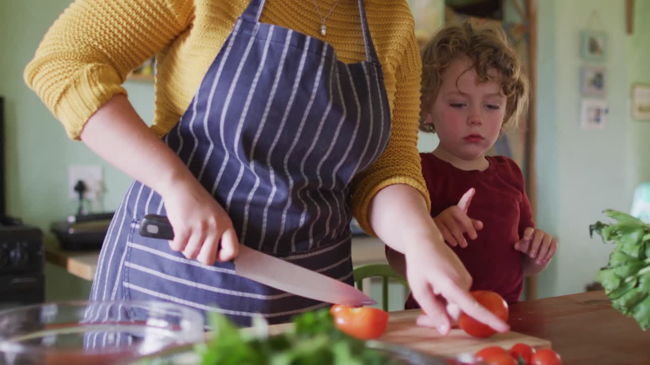madre y hijo caucásicos felices cortando verduras en la cocina