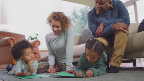 Großeltern-Sitzen-Zu-Hause-Mit-Enkelkindern-Auf-Dem-Boden-Und-Zeichnen-Gemeinsam-Ein-Bild