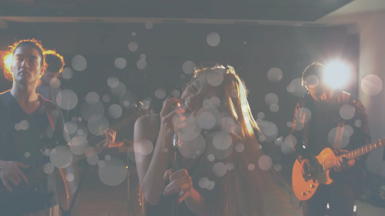 Female singer whipping hair gripping mic stand while band rehearsing, bokeh discs appearing onstage