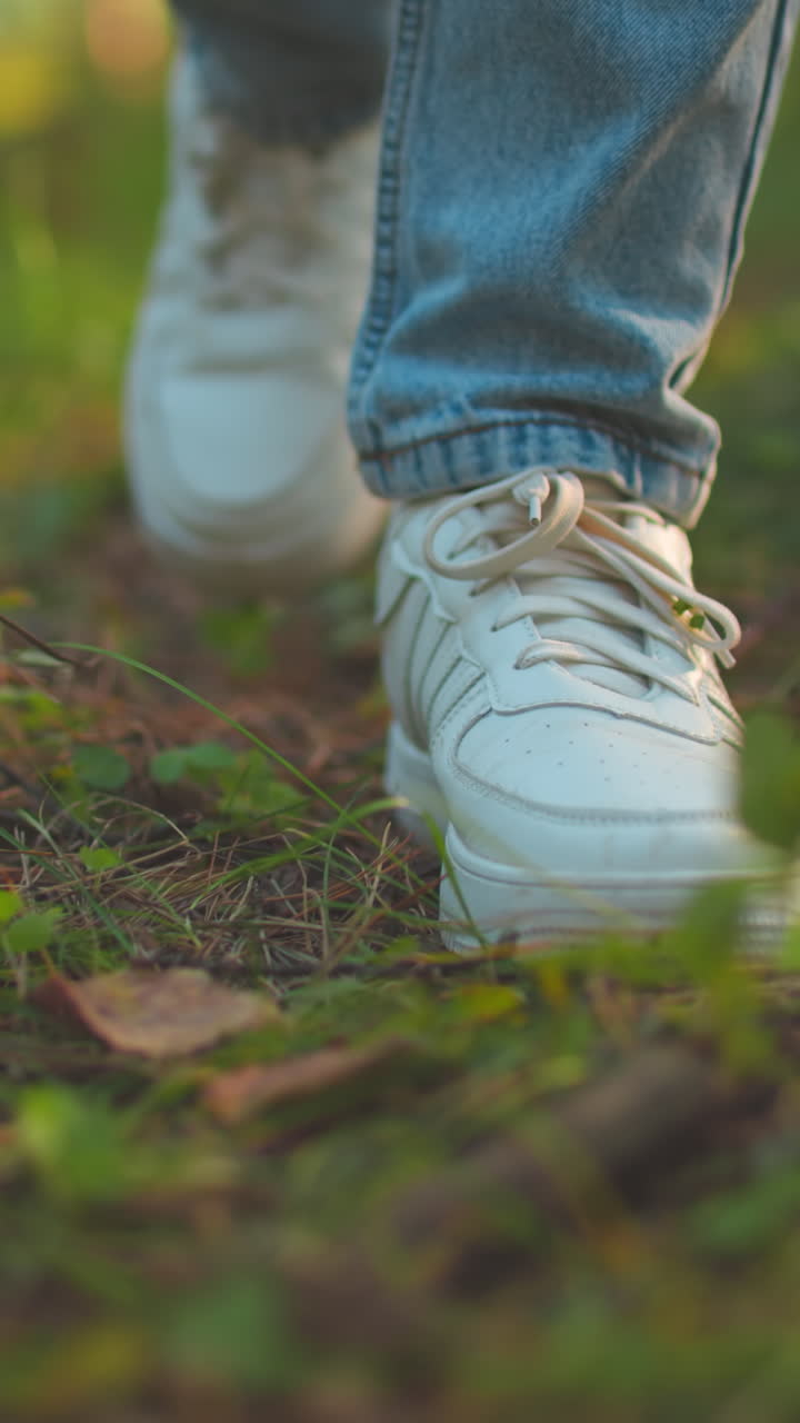 Close-up of individual s legs as they walk through lush forest path, wearing white sneakers and blue jeans, stepping gently on forest floor covered in twigs and small plants