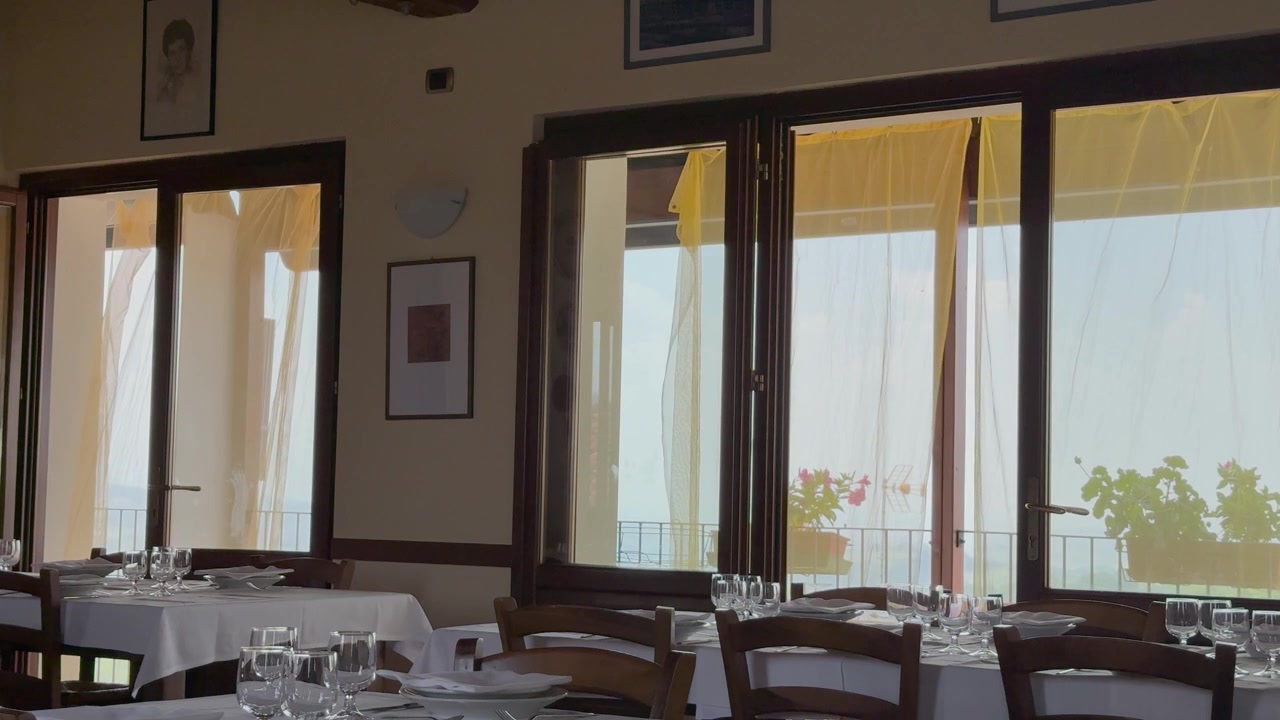 Inquadratura ampia statica di una sala da pranzo di ristorante vuota con tovaglie bianche e luce naturale