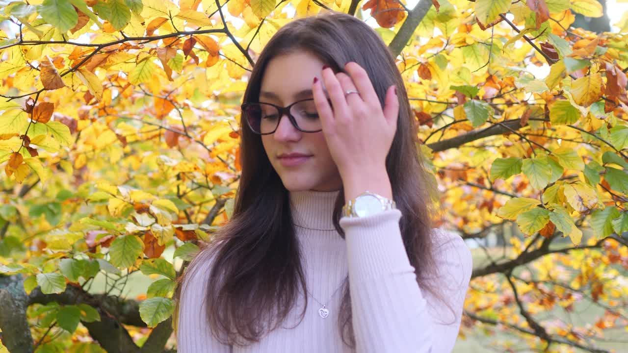 retrato de una adolescente feliz frente al follaje de un árbol verde amarillo en un brillante día de otoño, de cerca en cámara lenta